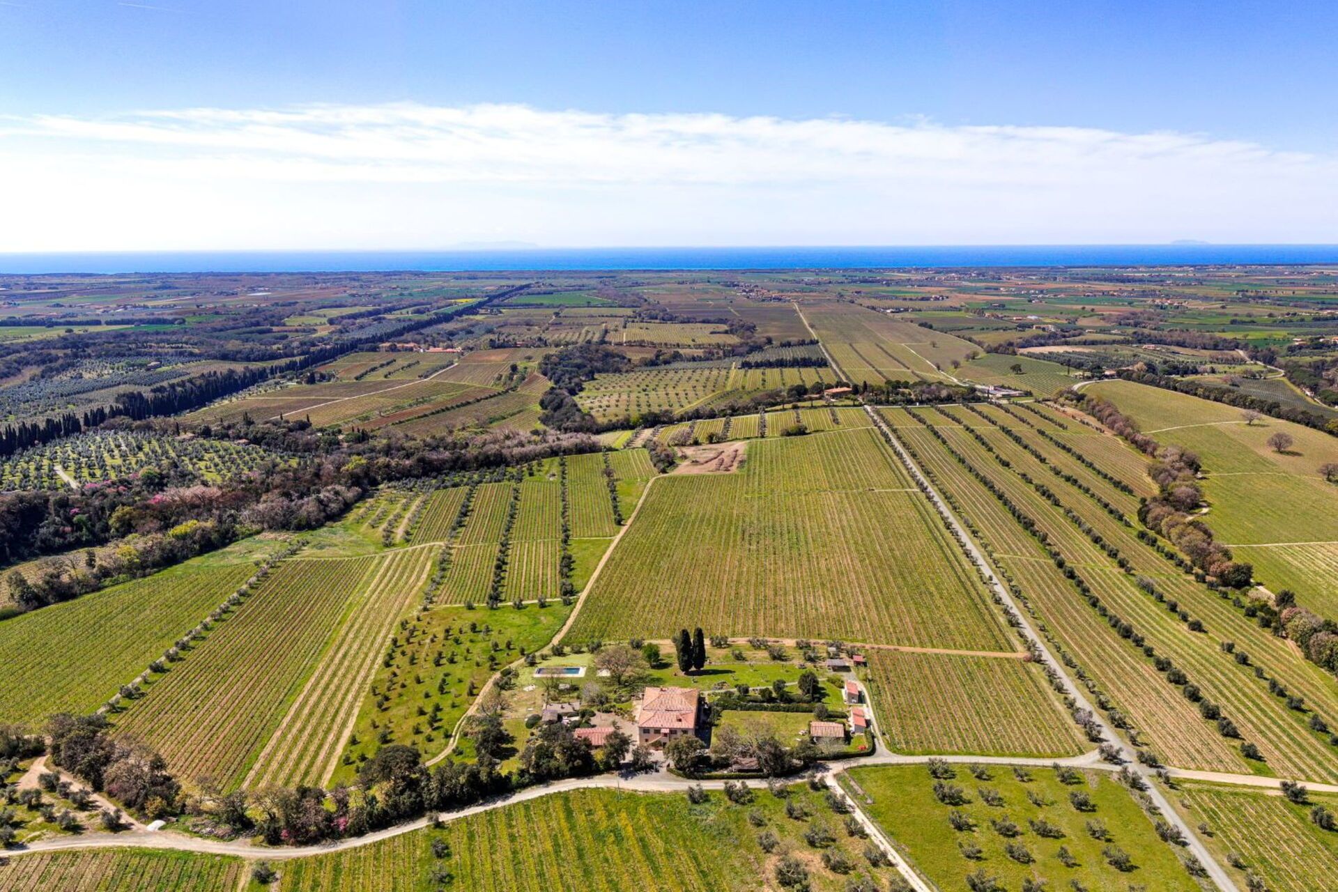 An aerial view of a rural landscape with fields, a small cluster of buildings, and a clear sky.