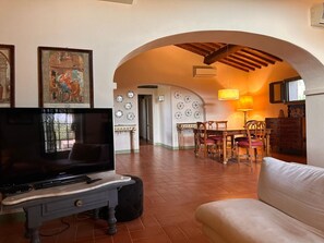 Ein Wohnzimmer mit Fernseher, einer Couch und einem Essbereich mit Stühlen und einem Tisch.