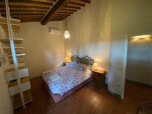 A bedroom with a bed, bedside lamps, a wooden ceiling, and a staircase. - Villa Stalletta Hot Tub by Geco Vacation Rentals (Bolgheri)