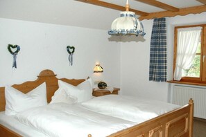 Ein Schlafzimmer mit einem hölzernen Bett, weißer Bettwäsche, einem Nachttisch mit Lampe und einem Fenster mit Vorhängen.