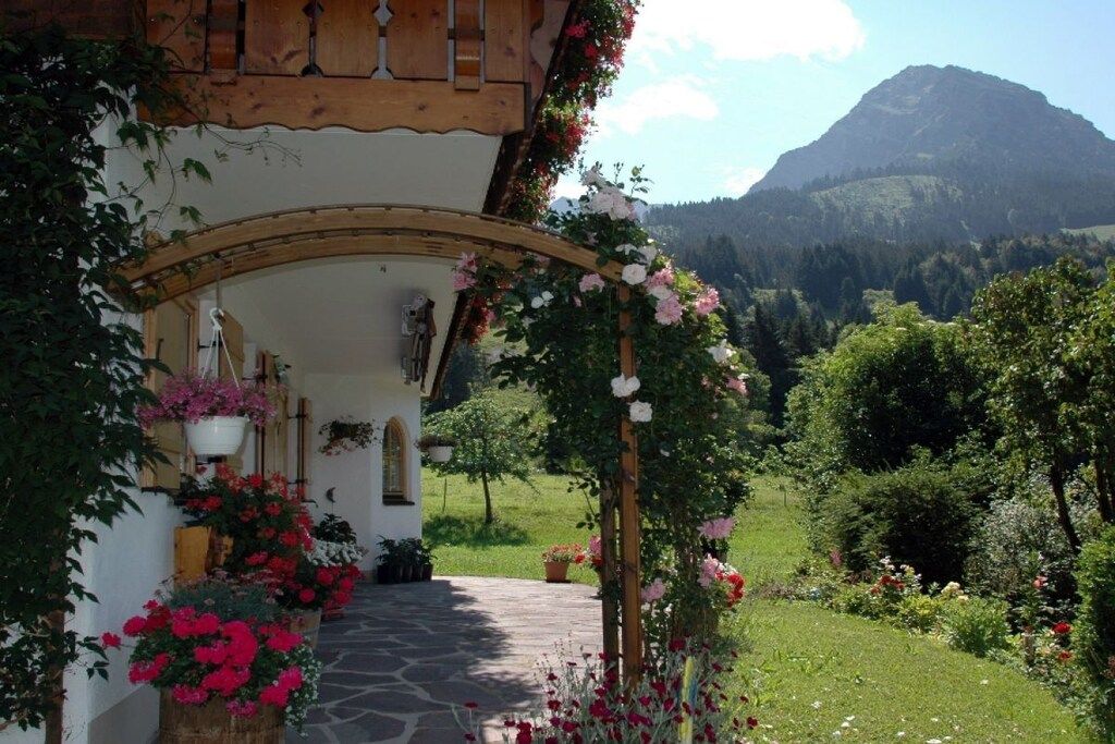 A rustic building with a stone pathway leading to a wooden archway adorned with flowers.