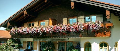 Un chalet traditionnel doté d’un balcon orné de fleurs, d’une terrasse en pierre et de plantes en pot.