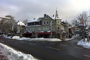 A two-story building with a red awning, a church steeple, and a snow-covered street. - Holiday apartment with 1 bedroom (Braunlage)