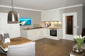 A modern kitchen with white cabinets, a wooden dining table, and a television displaying a scenic view. - Holiday apartment with 1 bedroom (Braunlage)