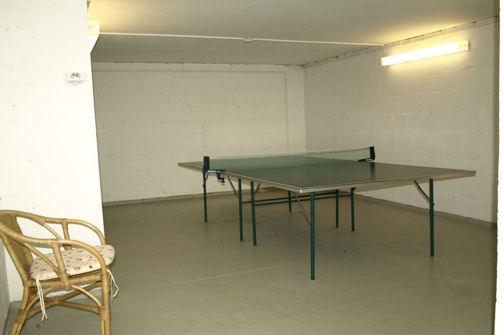 Een kamer met een tafeltennistafel, een rieten stoel en een witte muur.