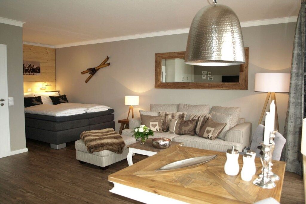 A modern bedroom with a bed, a sofa, a wooden coffee table, and a hanging lamp.