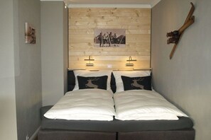 Een bed met een houten hoofdbord, twee bedlampen en een foto van skiërs.