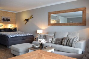 A modern bedroom with a bed, a sofa, a coffee table, and a large mirror. - Holiday apartment with 1 bedroom (Braunlage)
