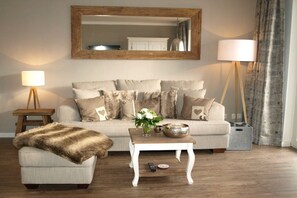 A living room with a sofa, a coffee table, a lamp, and a mirror on the wall. - Holiday apartment with 1 bedroom (Braunlage)