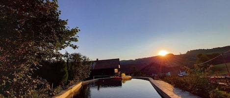 Una piscina con cubierta de madera, rodeada de árboles y una casa al fondo.