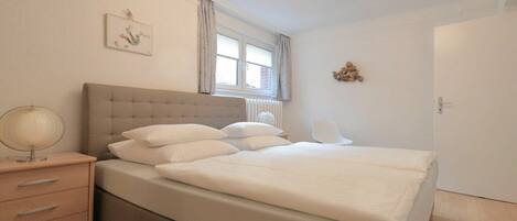 A bedroom with a bed, bedside table, lamp, and a window with curtains.