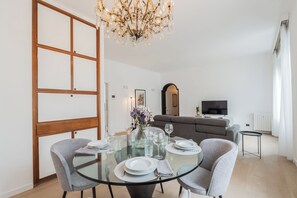 Un comedor moderno con una mesa de vidrio, sillas tapizadas en gris y un candelabro.
