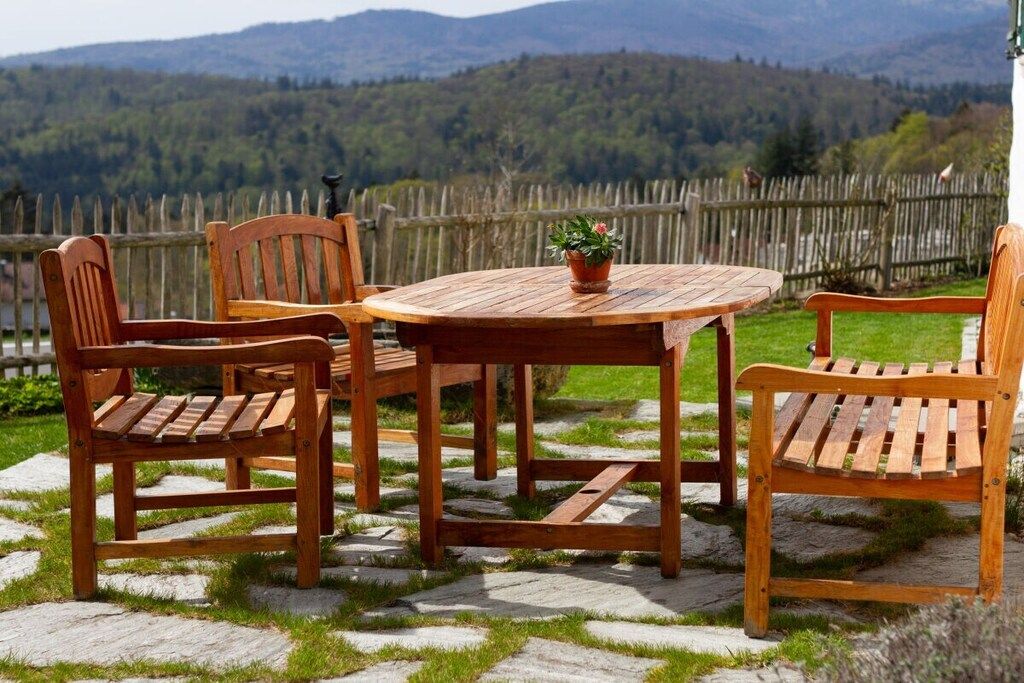 A wooden outdoor seating area with a table and chairs, surrounded by a stone-paved patio.