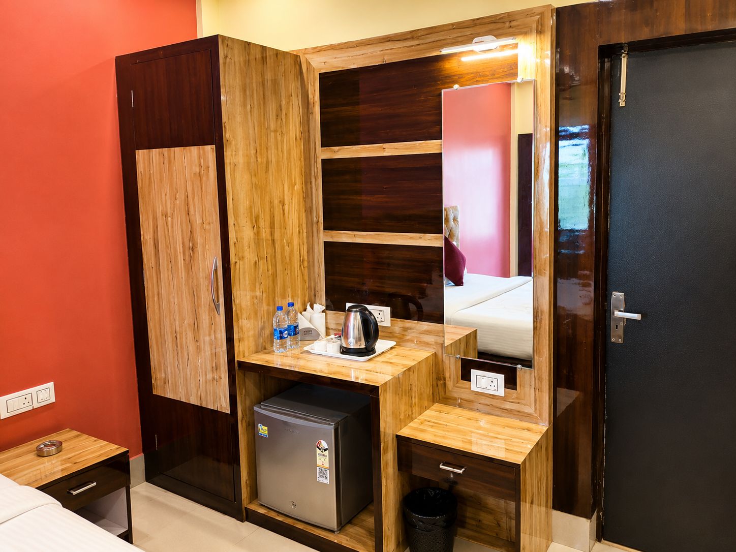 Una habitación de hotel compacta con un armario de madera, una pequeña kitchenette, una cama y un espejo.