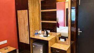 Una habitación de hotel compacta con un armario de madera, una pequeña kitchenette, una cama y un espejo.