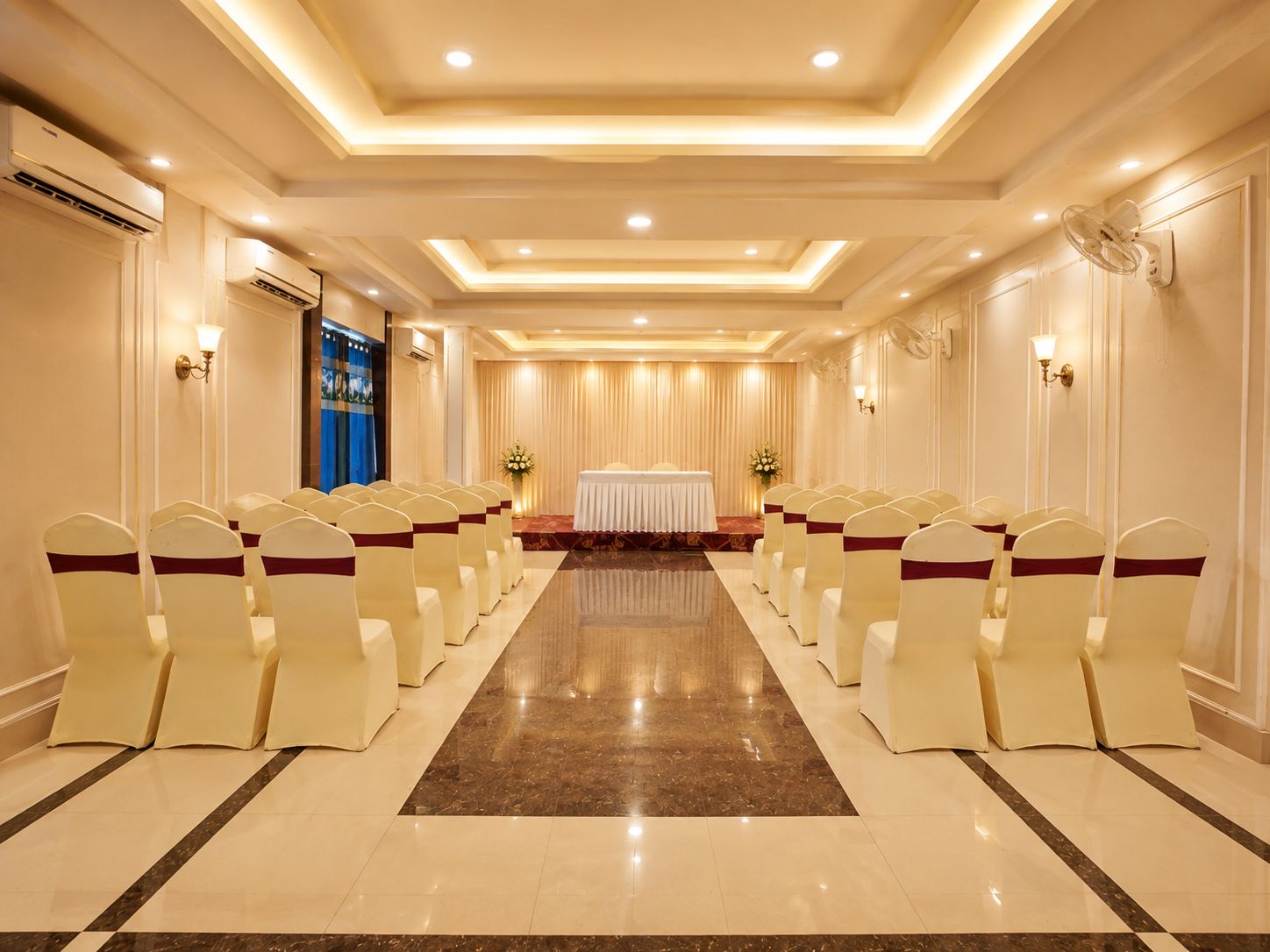 Un salón de conferencias con filas de sillas, un escenario con una mesa e iluminación en la pared.