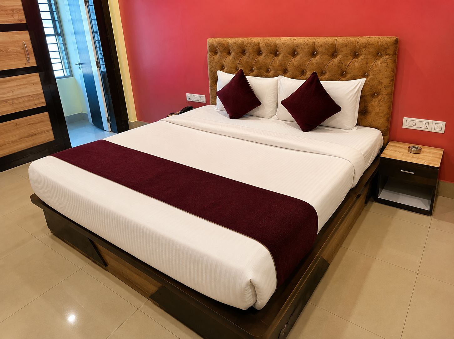A hotel room with a large bed, a wooden headboard, two bedside tables, and a red wall.