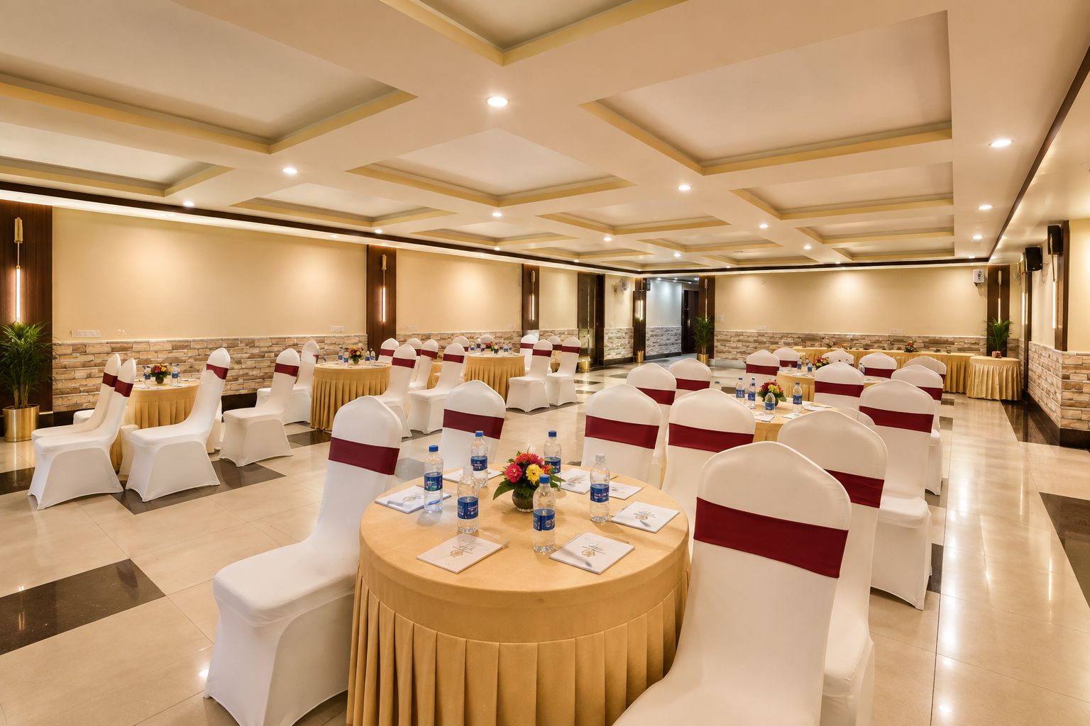 Une salle de conférence avec des tables rondes, des chaises blanches ornées de rubans rouges et un sol ciré.