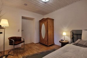 Ein Schlafzimmer mit einem Bett, einem Holzschrank, einem Stuhl, einem Nachttisch und einer Lampe.