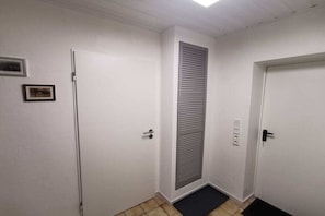 Ein Flur mit weißen Wänden, einer Tür mit Lamellen, einer Fußmatte und einem kleinen gerahmten Bild an der Wand.