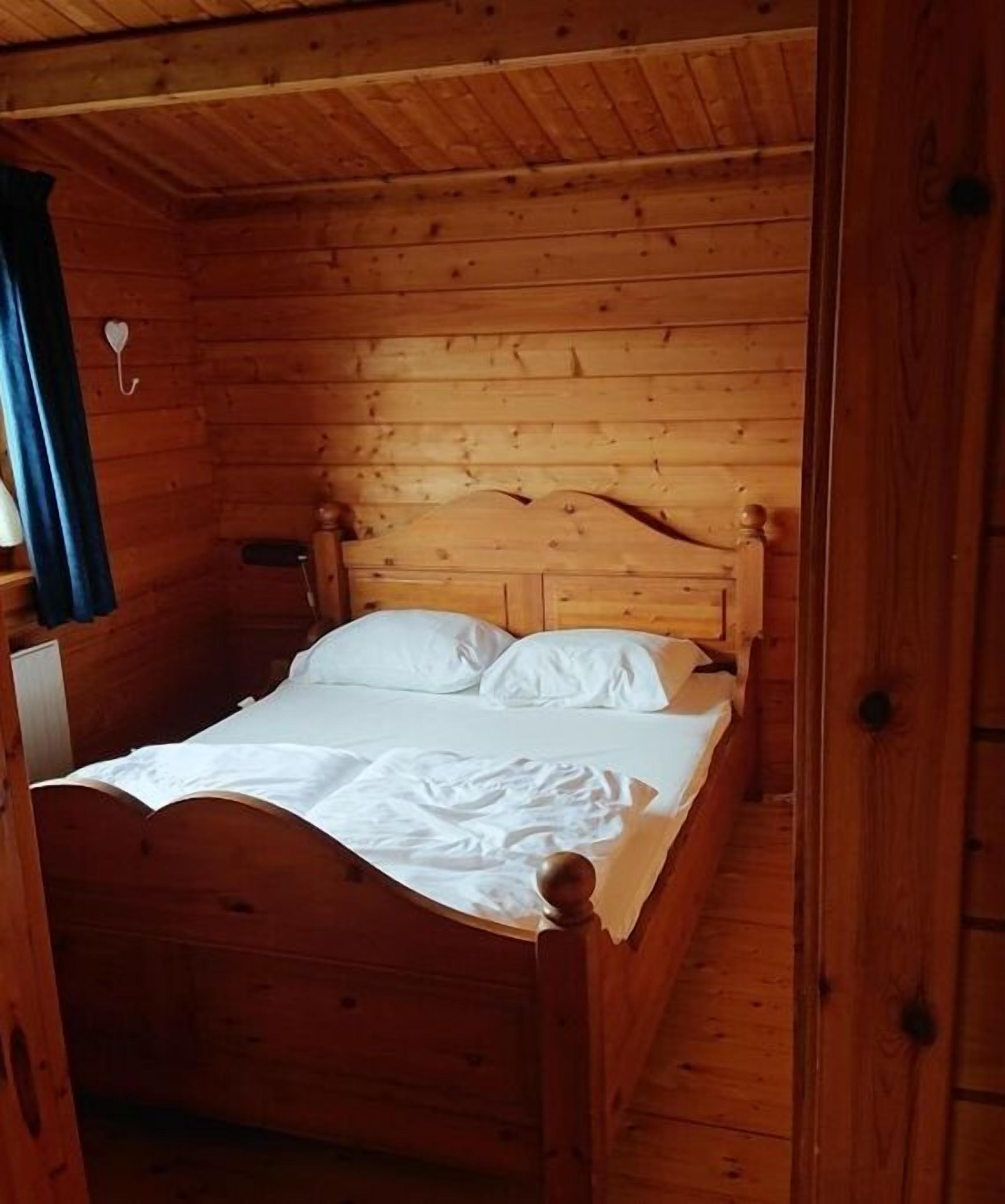Uma cama de madeira em um quarto estilo cabana, com uma cabeceira simples e uma mesinha de cabeceira.
