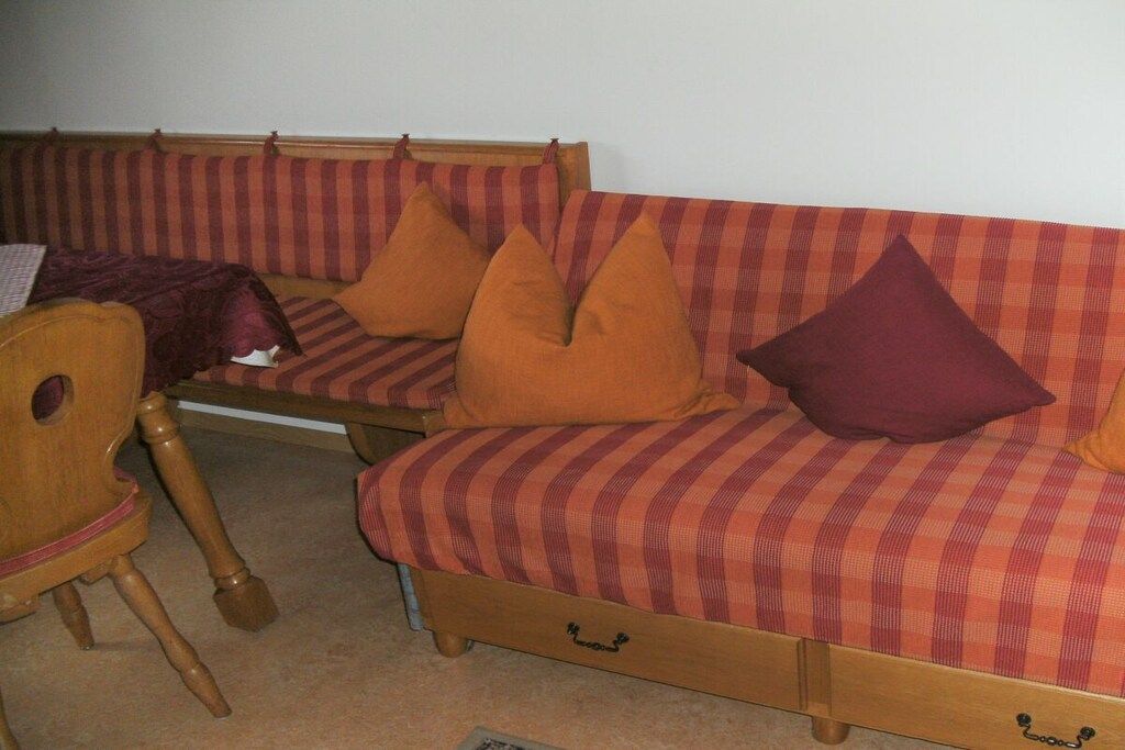 En hjørnesofa med stribet betræk og mange puder, en træstol og et lille bord med pude.