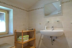 Un baño con un lavamanos blanco, un espejo encima y un estante de madera con toallas.