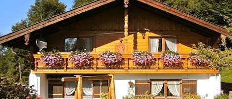 A wooden chalet with a balcony, windows, and a garden.