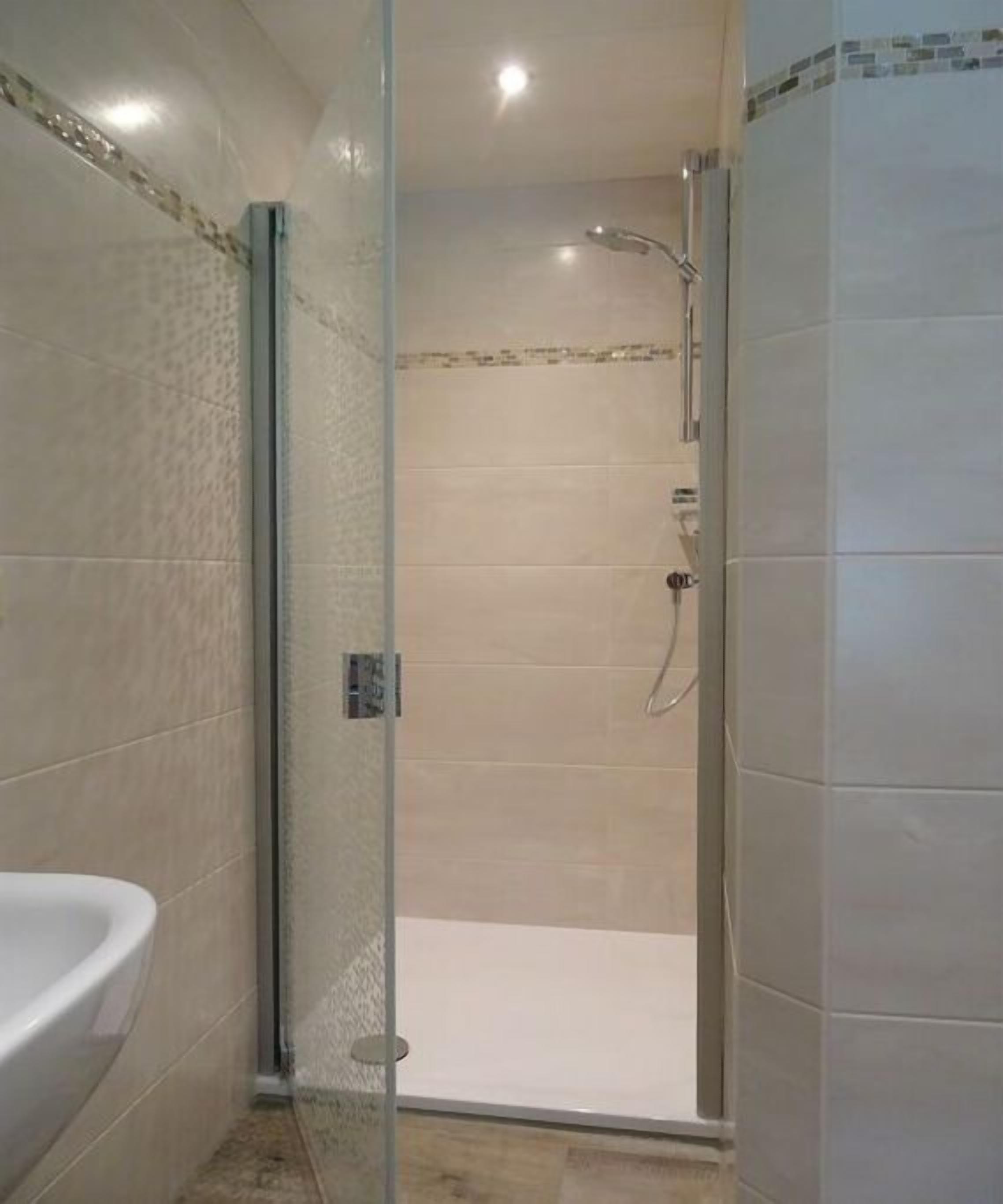 Ein Duschbereich mit Glasabtrennung und eine weiße Badewanne links davon.