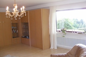 Ein Zimmer mit Holzschrank, einer Kristallleuchtre, einem Fenster mit Blick auf Grünflächen und einer Heizung.