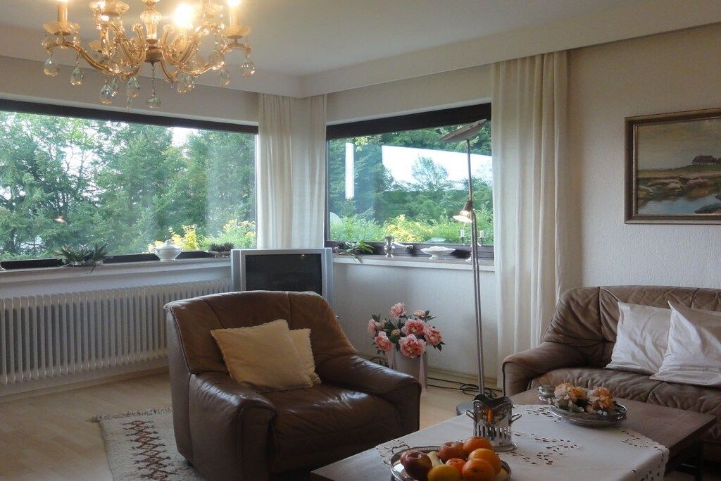 A living room with a brown leather sofa, a brown armchair, a coffee table with fruit, a vase with flowers, and a painting on the wall.
