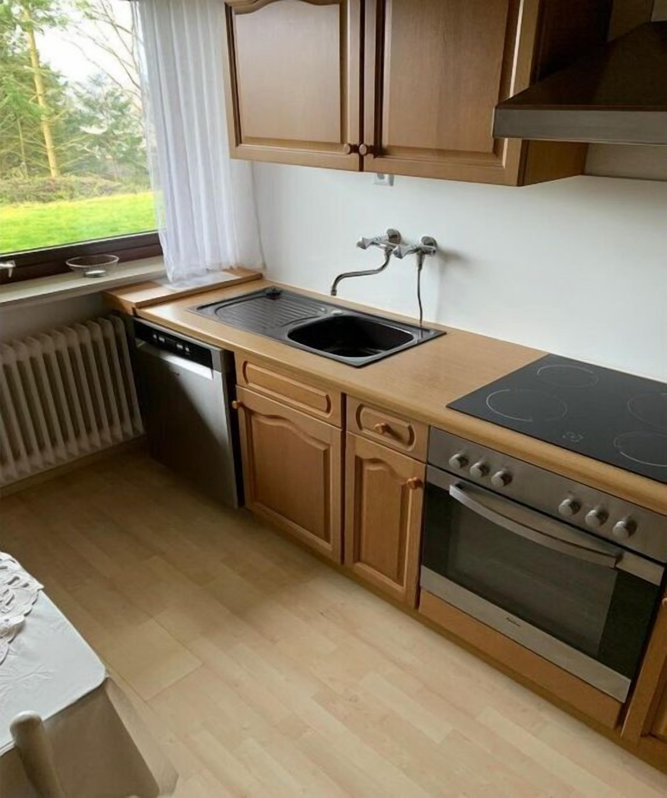 Una cucina compatta con mobili in legno, forno integrato e una finestra vista verde.