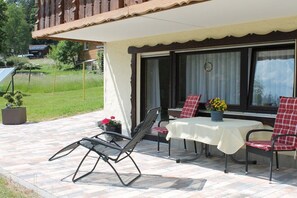 An outdoor patio with a table and chairs, a potted plant, and a view of a house in the background. - Holiday apartment with 2 bedrooms (Baiersbronn-Obertal)
