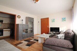 Un espacio habitable compacto con kitchenette, un sofá, un televisor y una mesa de comedor.