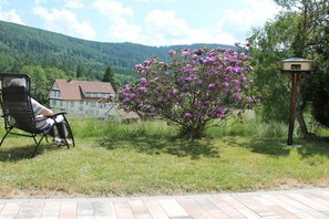 A person seated on a chair in a grassy area with a house and mountains in the background. - Holiday apartment with 2 bedrooms (Baiersbronn-Obertal)