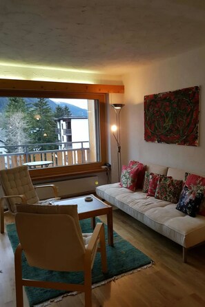 Ein Wohnzimmer mit einer Couch, Sesseln, einem Tisch, einer Lampe und einem Gemälde.