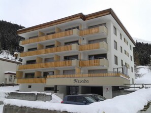 Ein mehrstöckiges Gebäude mit Balkonen, einem Namen Schild und einem Parkplatz mit Schnee.