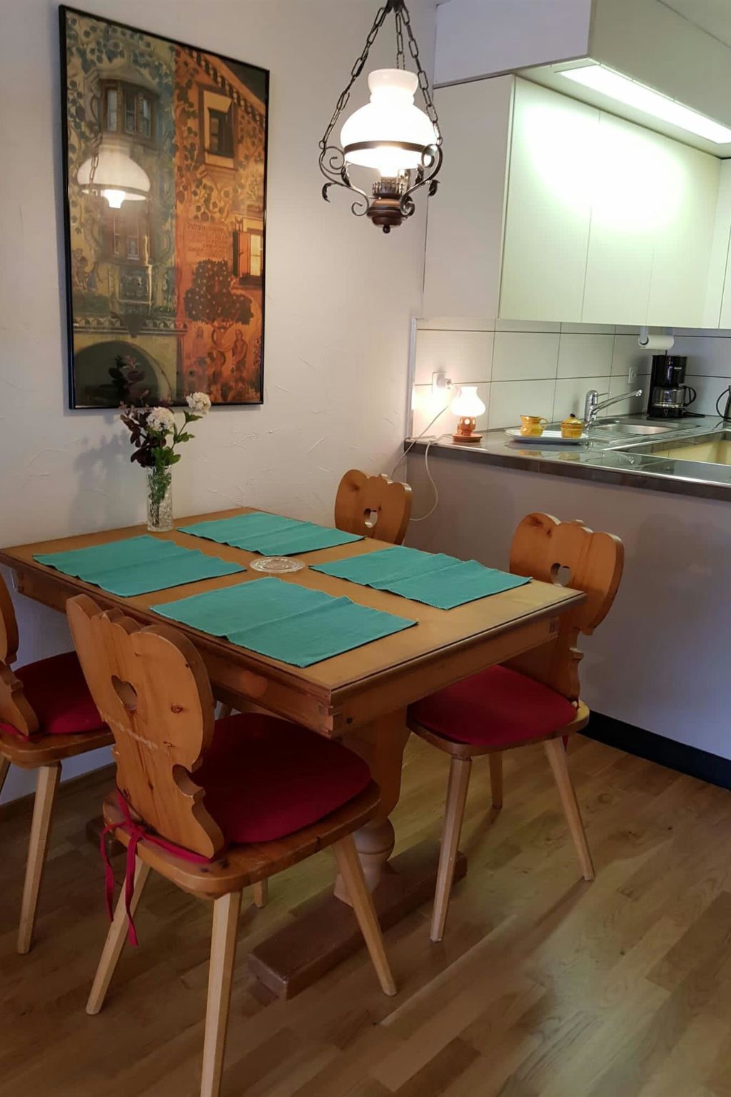 Uma sala de jantar com mesa de madeira, quatro cadeiras e um vaso de flores.