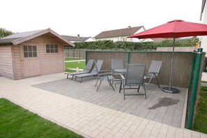A patio area with a wooden shed, a table with four chairs, and a red umbrella. - Holiday apartment with 2 bedrooms (Cadzand-Bad)