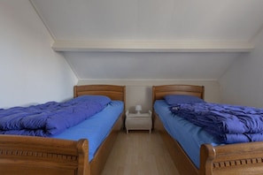 A room with two wooden beds, each with a blue bedspread, a small white nightstand, and a white lamp between the beds. - Holiday apartment with 2 bedrooms (Cadzand-Bad)