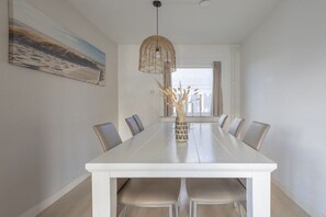 A dining area with a white table, six chairs, a hanging light fixture, and a window with curtains. - Holiday apartment with 2 bedrooms (Cadzand-Bad)