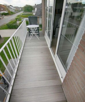 Un balcon avec une table et des chaises, un vélo et une vue sur la rue.