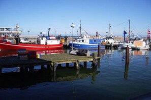Ein Yachthafen mit mehreren Schiffen an den Liegeplätzen, einer hölzernen Mole und blauem Himmel.