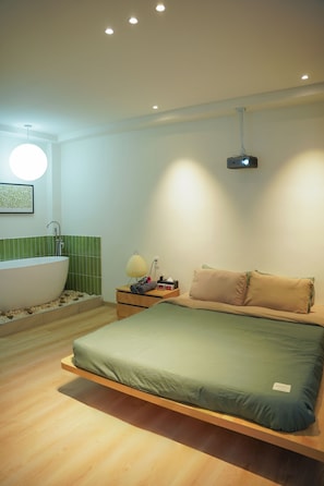 Une chambre à coucher moderne avec un lit, une table de chevet, un projecteur fixé au mur et une baignoire.