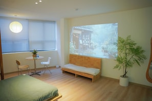 A room with a bed, a small table with chairs, a sofa, a large window with a projection, and a potted plant. - Benri Homestay (Cau Kieu)