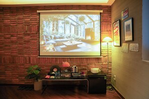 Une pièce avec un mur en briques, un écran de projection affichant une image d’un salon chaleureux, une lampe et quelques objets posés sur une table.