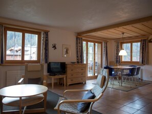 A room with a television, a wooden dresser, a dining table with chairs, and large windows. - Heidblick Appartement/Fewo, Dusche oder Bad, WC 3½-Zimmerwohnung by Interhome (Klosters)
