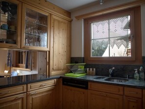 A kitchen with wooden cabinets, a window with lace curtains, and a sink. - Heidblick Appartement/Fewo, Dusche oder Bad, WC 3½-Zimmerwohnung by Interhome (Klosters)