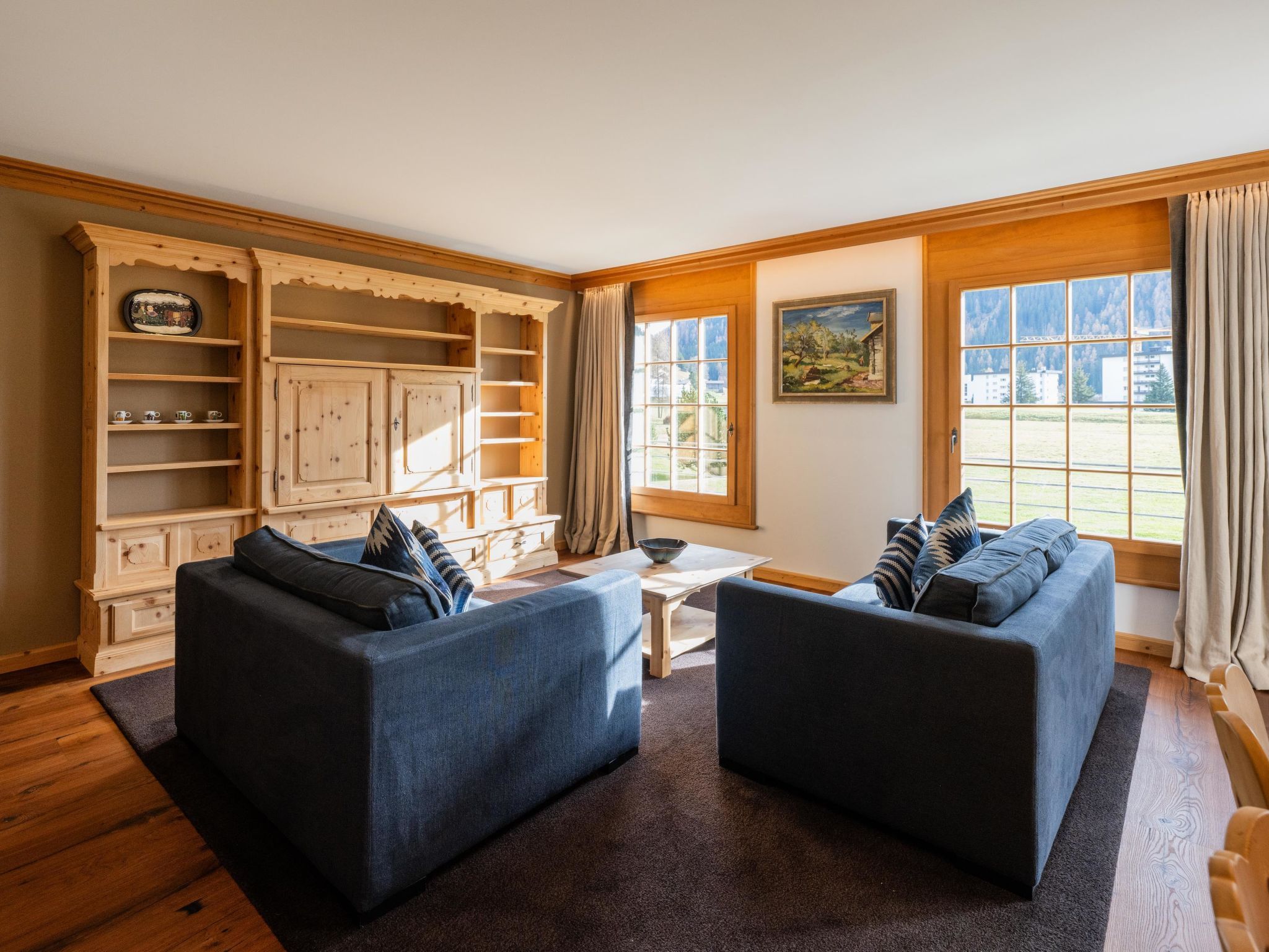 A room with two sofas, a wooden cabinet, a painting, and a window with curtains.