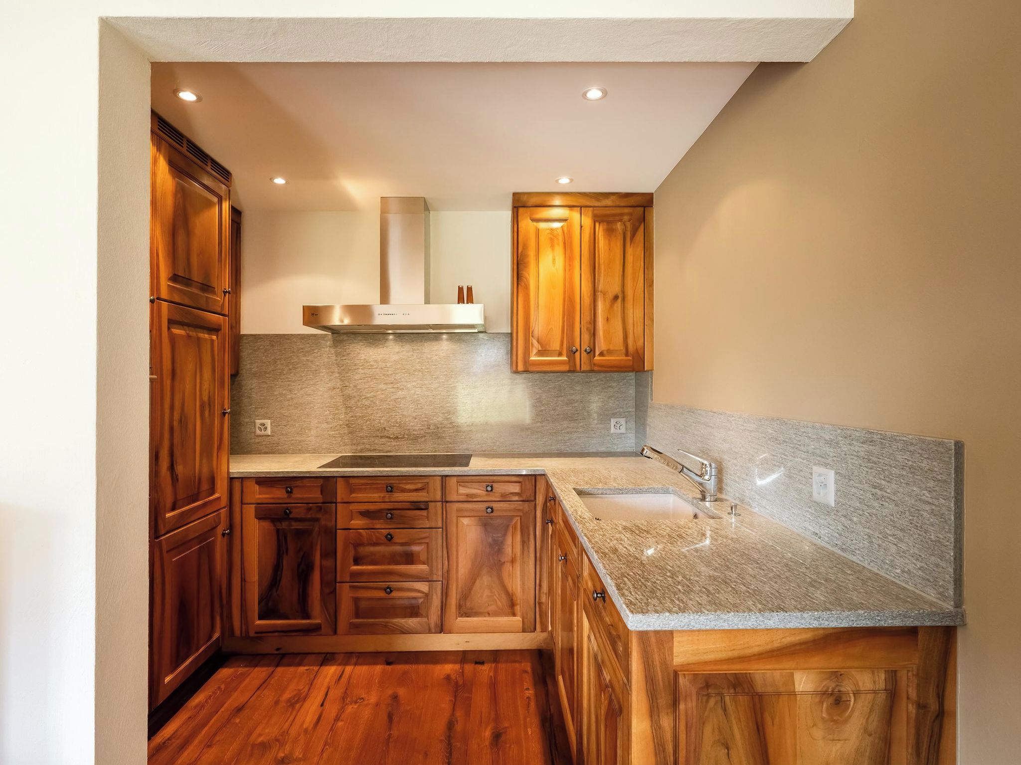 Cocina compacta con armarios de madera, encimera de granito y campana extractora de acero inoxidable.